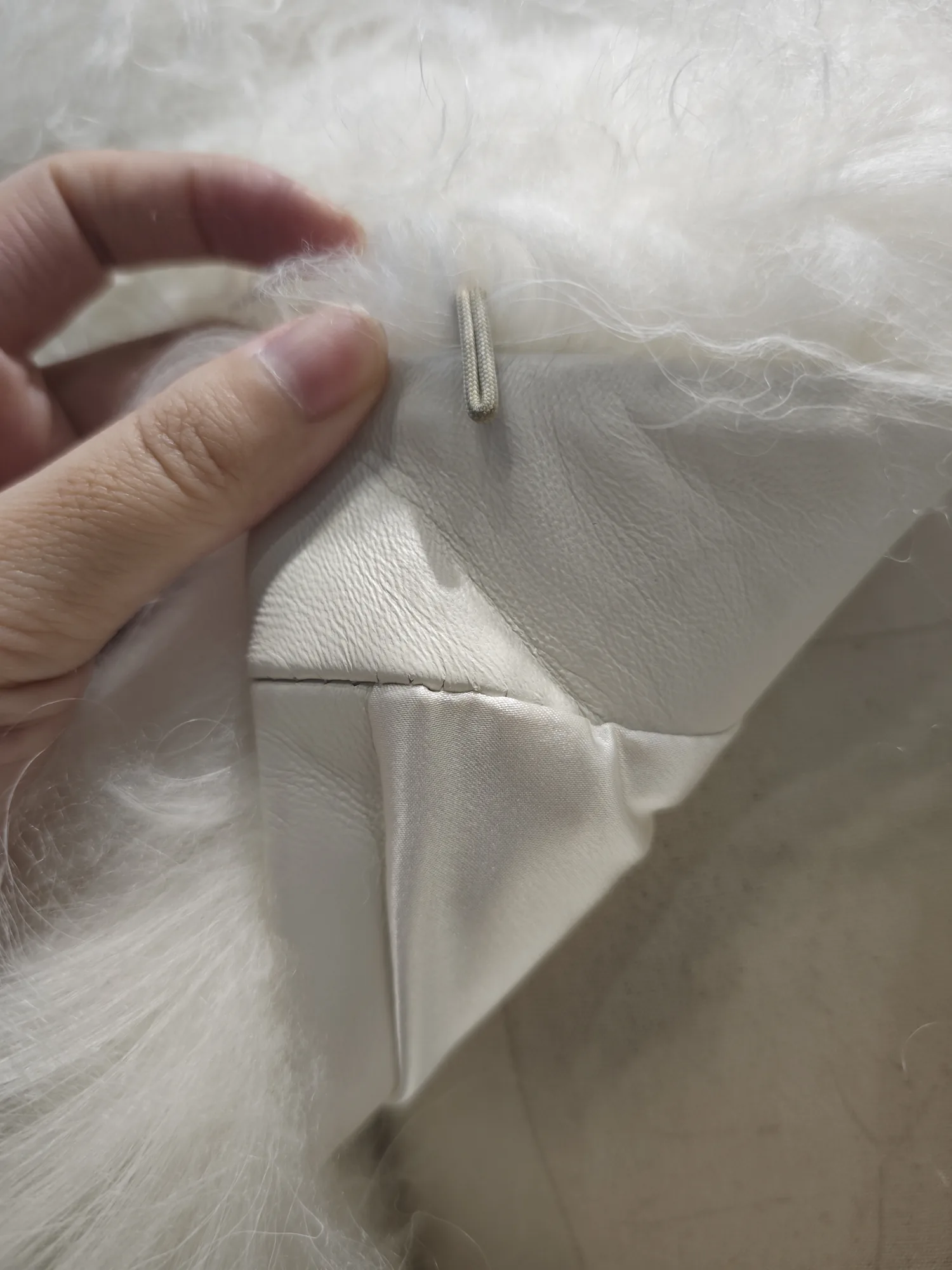 Close-up of the corded loop closure and leather facing inside a white curly lamb fur jacket